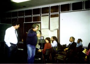 Room of people, some sitting in rows of seats and two men standing speaking