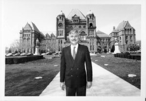 Reville in dark suit standing in front of Queen's Park