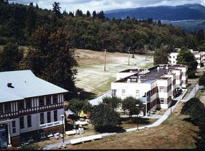 Cluster of institutional buildings on wooded hillside with mountains in the background