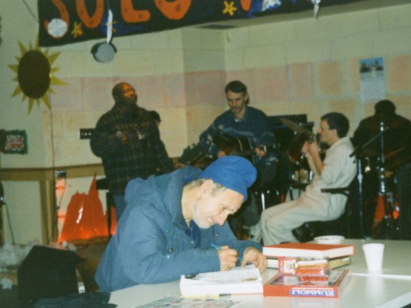 Members sitting at tables in PARC Drop-In with man at front sitting reading by himself at a table