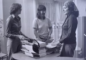 3 women standing together around a table filled with stacks of open library books