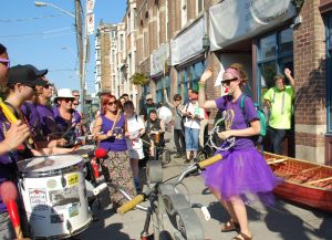 Photo d'été coloré à l'extérieur devant l'entrée de la communauté PARC. Des percussionnistes et musiciens forment un cercle.