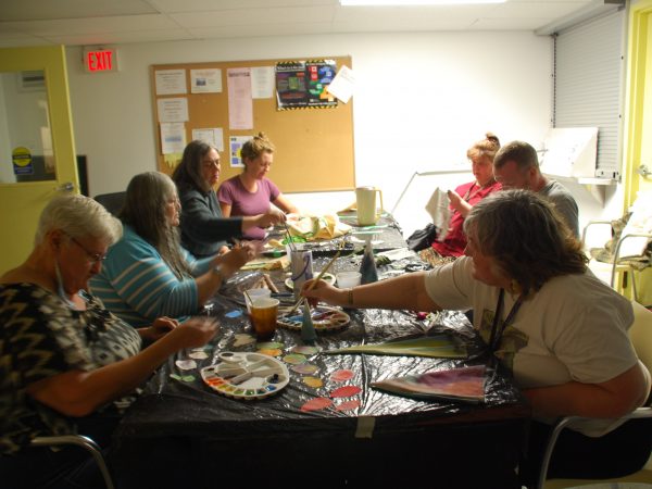 Group of seven Making Room participants sitting around table at creating art with paint and fabric