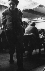 black and white photo of men sitting and standing in area with tables